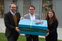 Die Architekten Michael Beck (Nova Architekten) Matthias Duhm (bmp architekten) überreichen Kita-Leiterin Melanie Jahn ein Geschenk zur Einweihung (v. links).